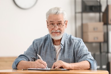 Photo of Senior man signing Last Will and Testament at table indoors