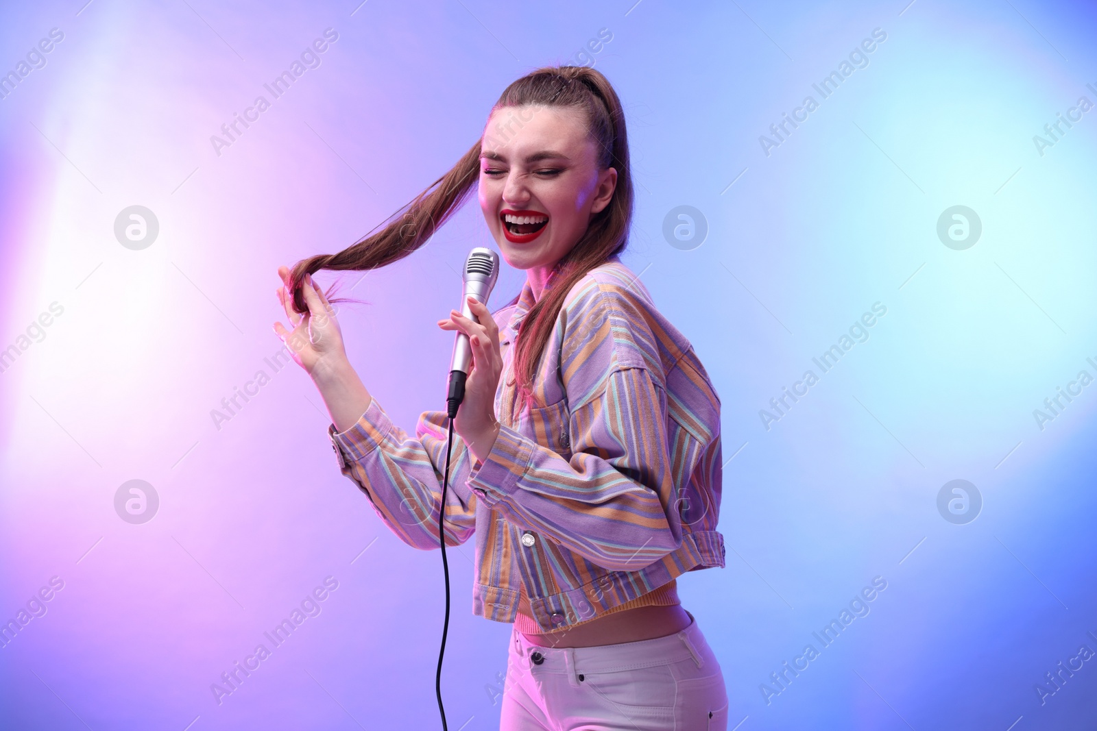 Photo of Emotional woman with microphone singing in color lights