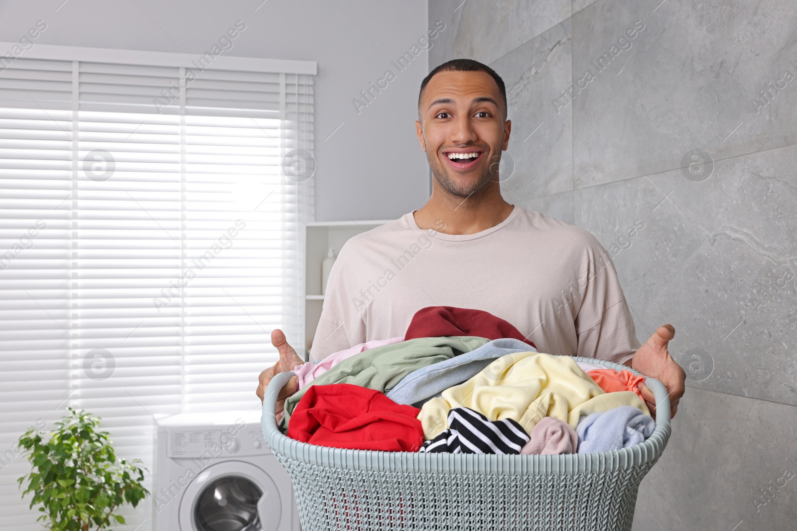Photo of Emotional man with basket full of laundry in bathroom. Space for text