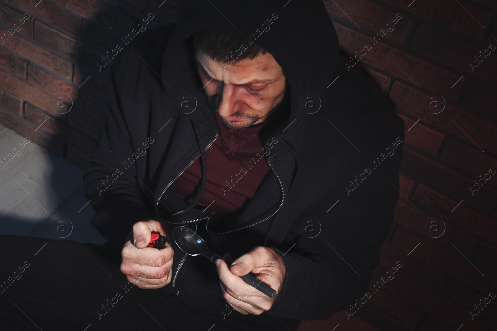 Photo of Man preparing drug with spoon and lighter near brick wall