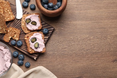 Photo of Tasty sandwiches with cream cheese and blueberries on wooden table, flat lay. Space for text