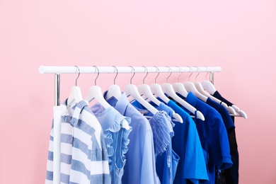 Rack with bright clothes on color background