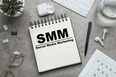 Image of Notebook with text SMM (Social media marketing) and other objects on grey table, flat lay
