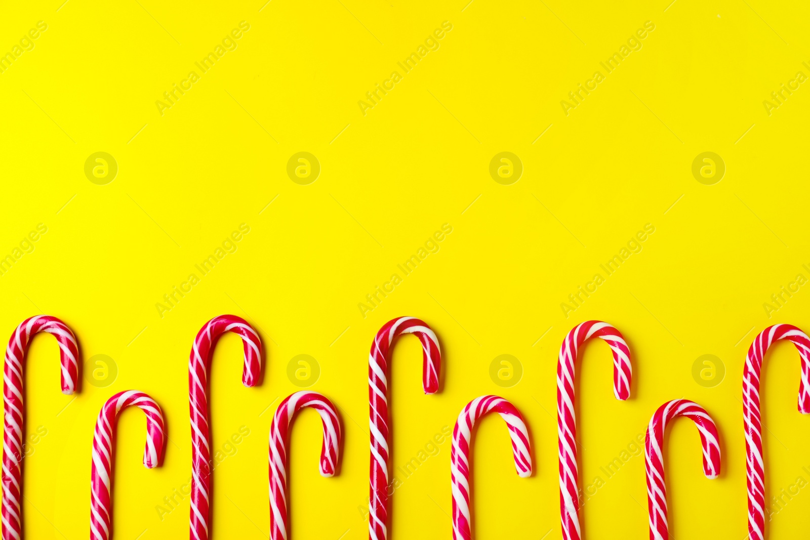Photo of Sweet Christmas candy canes on yellow background, flat lay. Space for text