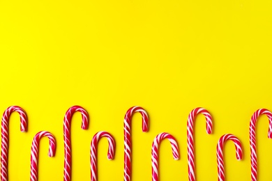 Photo of Sweet Christmas candy canes on yellow background, flat lay. Space for text