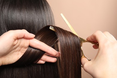 Hairdresser cutting client's hair with scissors on beige background, closeup