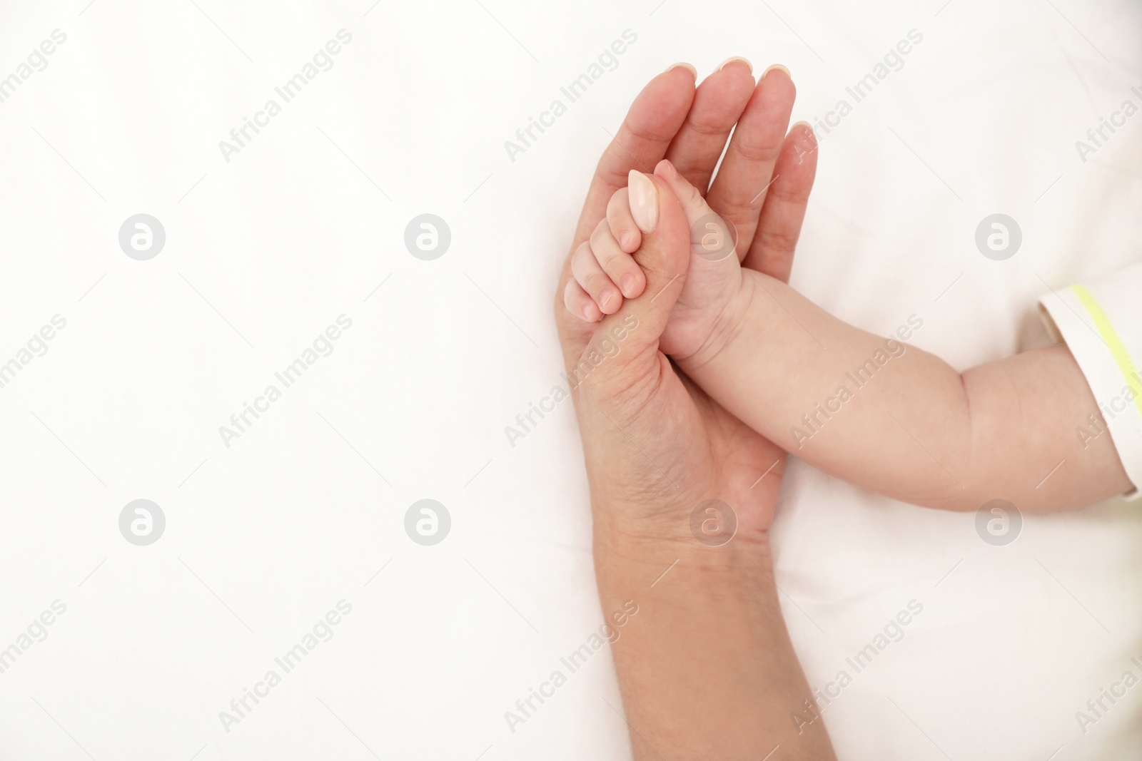 Photo of Mother holding her baby's hand on bed, top view. Space for text