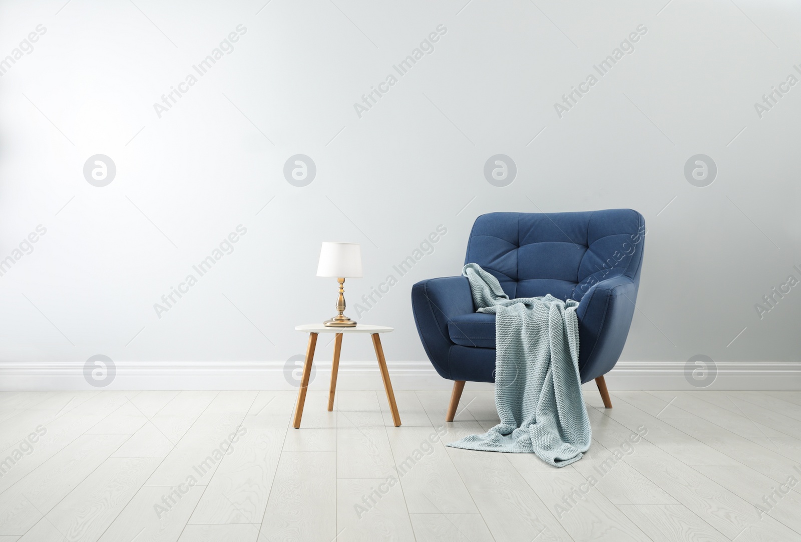 Photo of Stylish armchair with plaid, table and lamp near white wall. Interior design