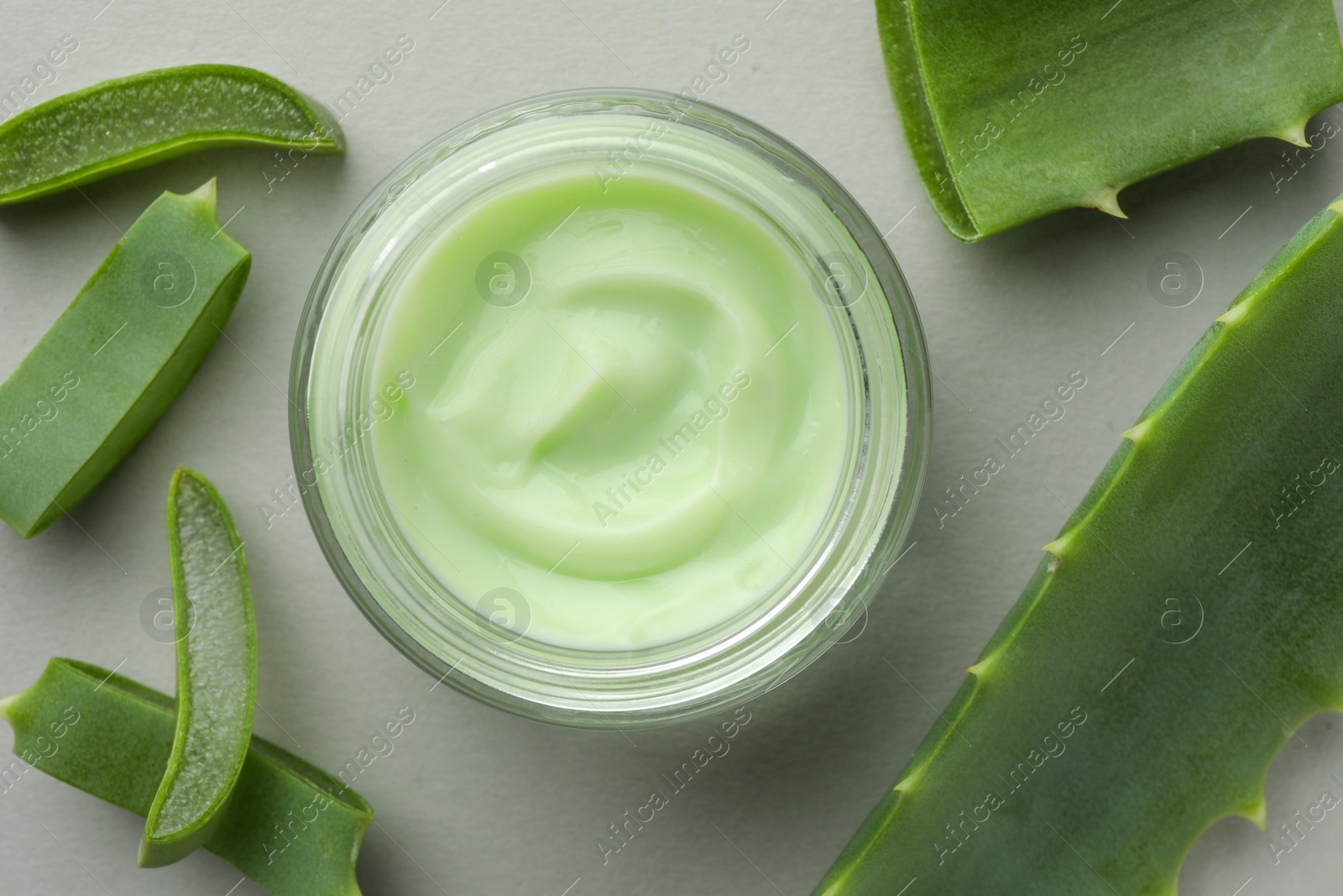 Photo of Jar with cream and cut aloe leaves on light grey background, flat lay