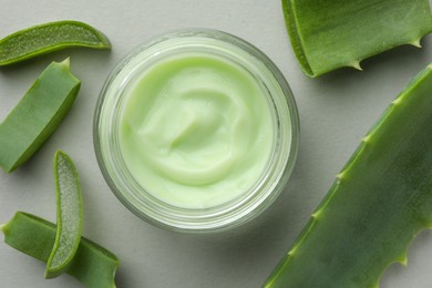 Photo of Jar with cream and cut aloe leaves on light grey background, flat lay