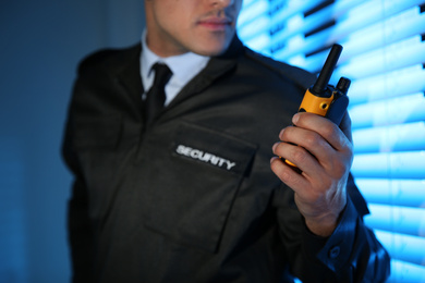 Professional security guard with portable radio set near window in dark room, closeup