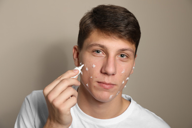 Photo of Teen guy with acne problem applying cream on beige background