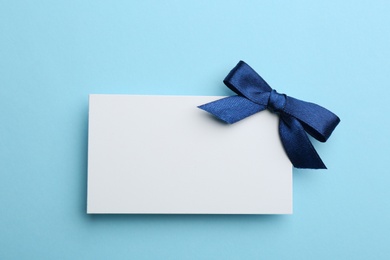 Photo of Gift card with bow on light blue background, top view. Mockup for design