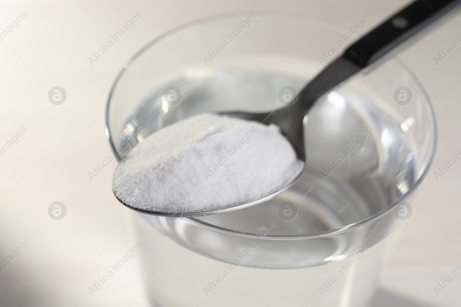 Photo of Glass of water and spoon with baking soda on light background, closeup