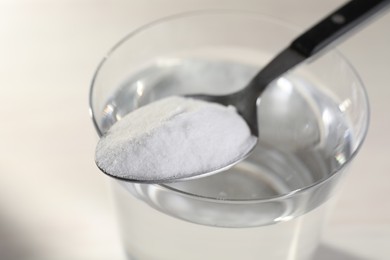 Glass of water and spoon with baking soda on light background, closeup