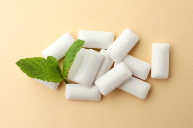 Photo of Tasty white chewing gums and mint leaves on beige background, top view