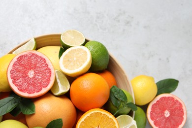 Photo of Different fresh citrus fruits and leaves in bowl on light table, flat lay. Space for text