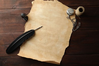 Sheet of old parchment paper, black feather, inkwell, rope and pocket chain clock on wooden table, flat lay