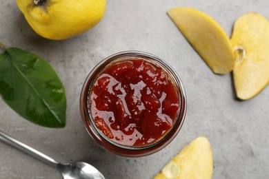 Photo of Delicious quince jam, fruits, leaves and spoon on grey table, flat lay
