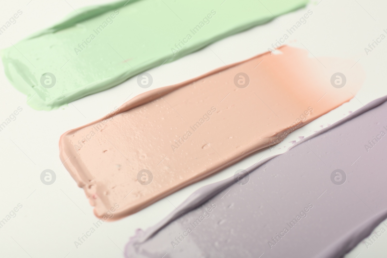 Photo of Strokes of pink, green and purple color correcting concealers on white background, closeup