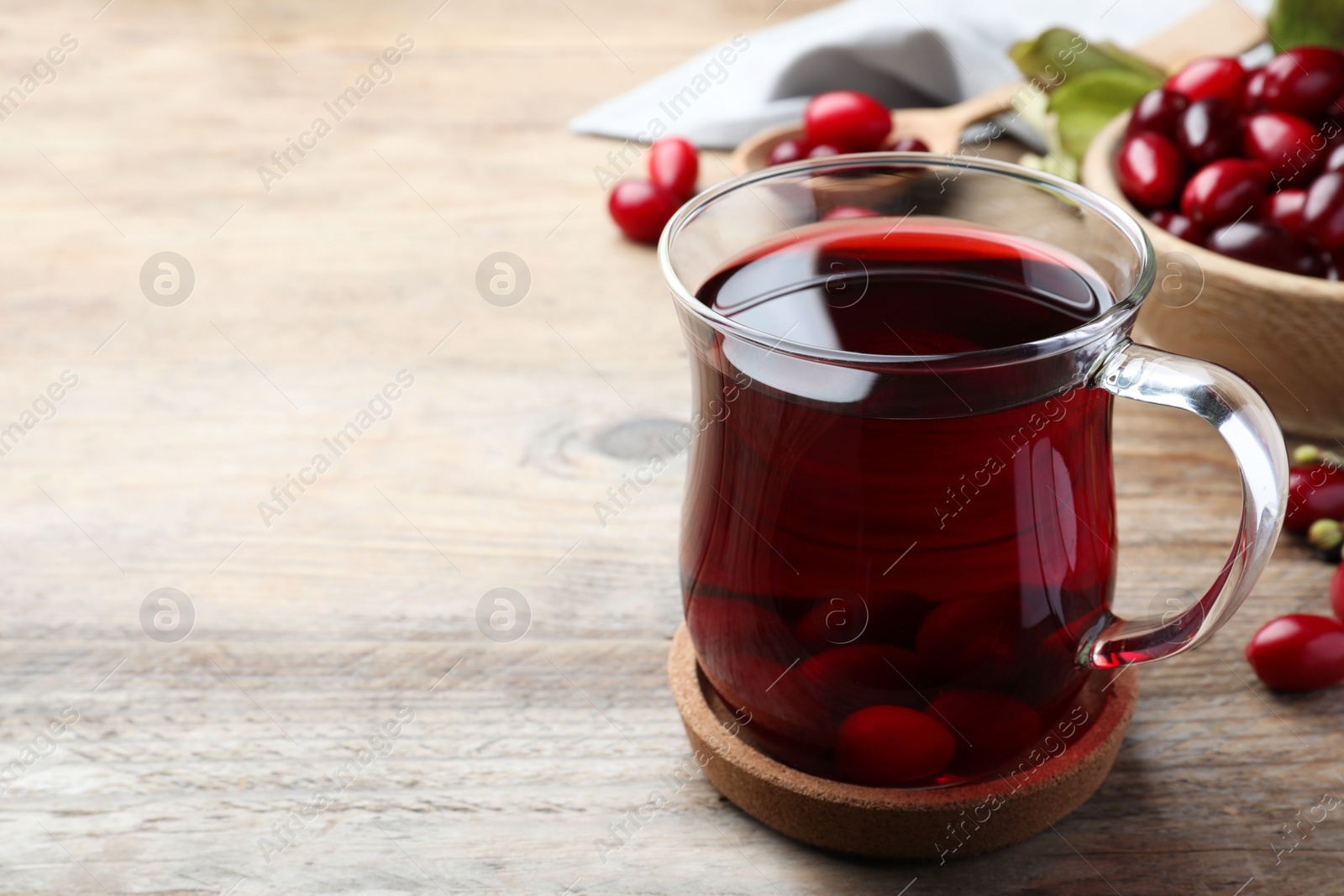 Photo of Glass cup of fresh dogwood tea with berries on wooden table. Space for text