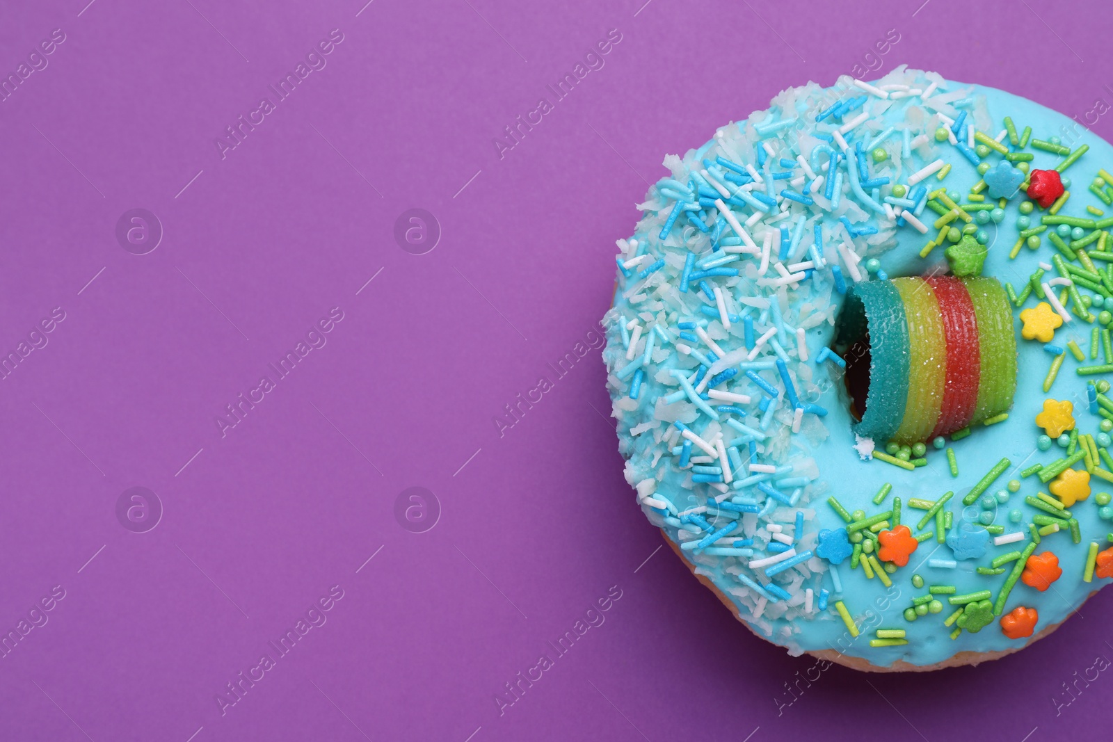 Photo of Sweet glazed donut decorated with sprinkles on purple background, top view and space for text. Tasty confectionery