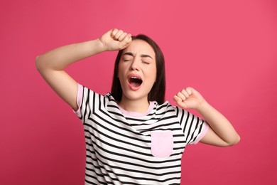 Young tired woman yawning on pink background