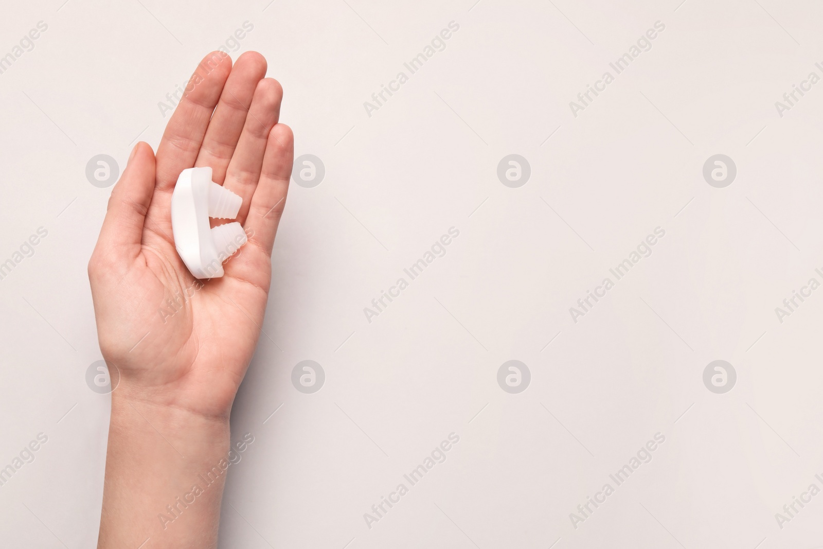 Photo of Woman holding anti-snoring device on light grey background, top view. Space for text