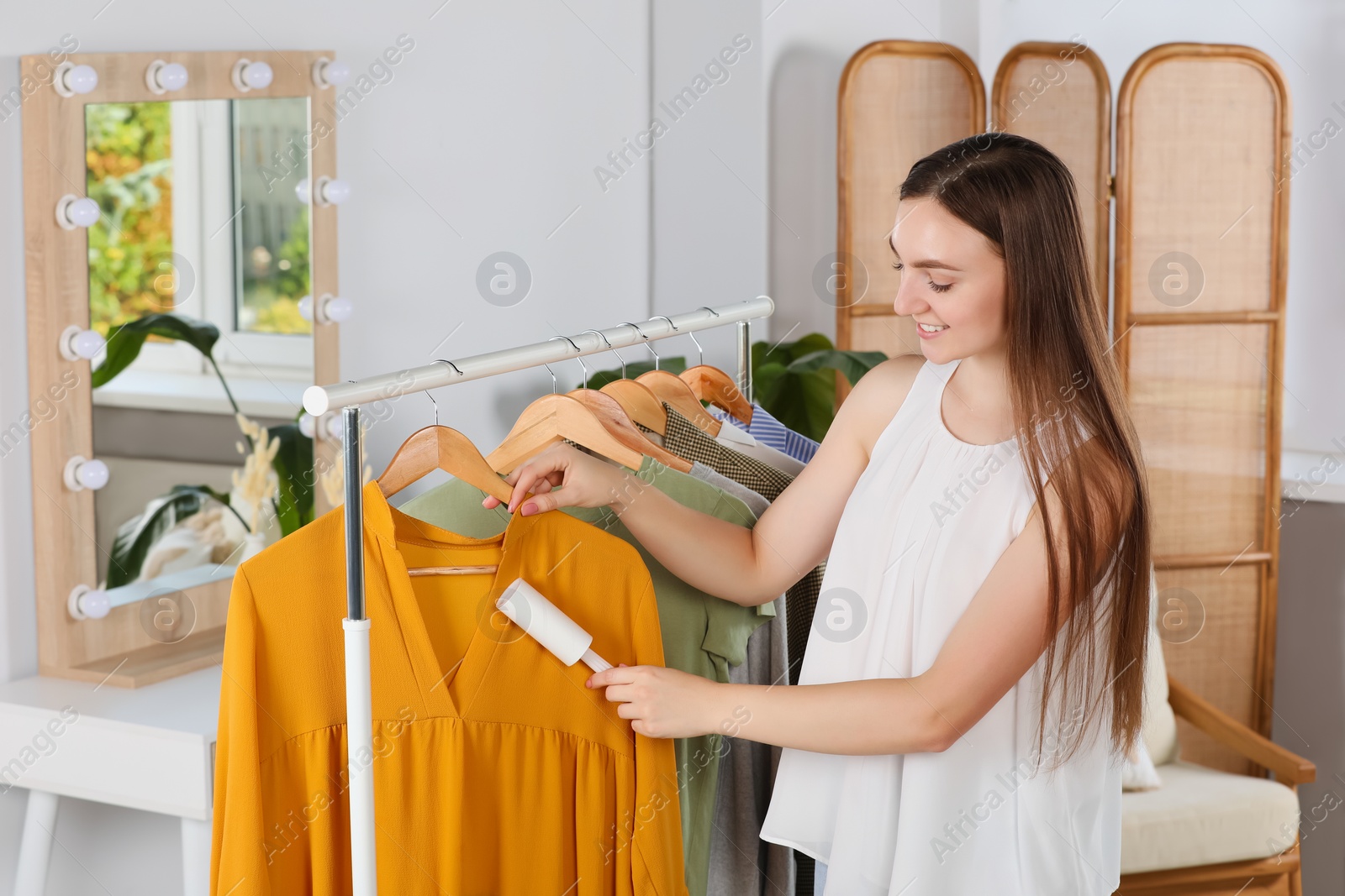 Photo of Young woman cleaning clothes with adhesive lint roller indoors