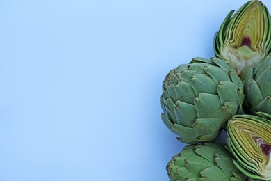 Photo of Cut and whole fresh raw artichokes on light blue background, flat lay. Space for text