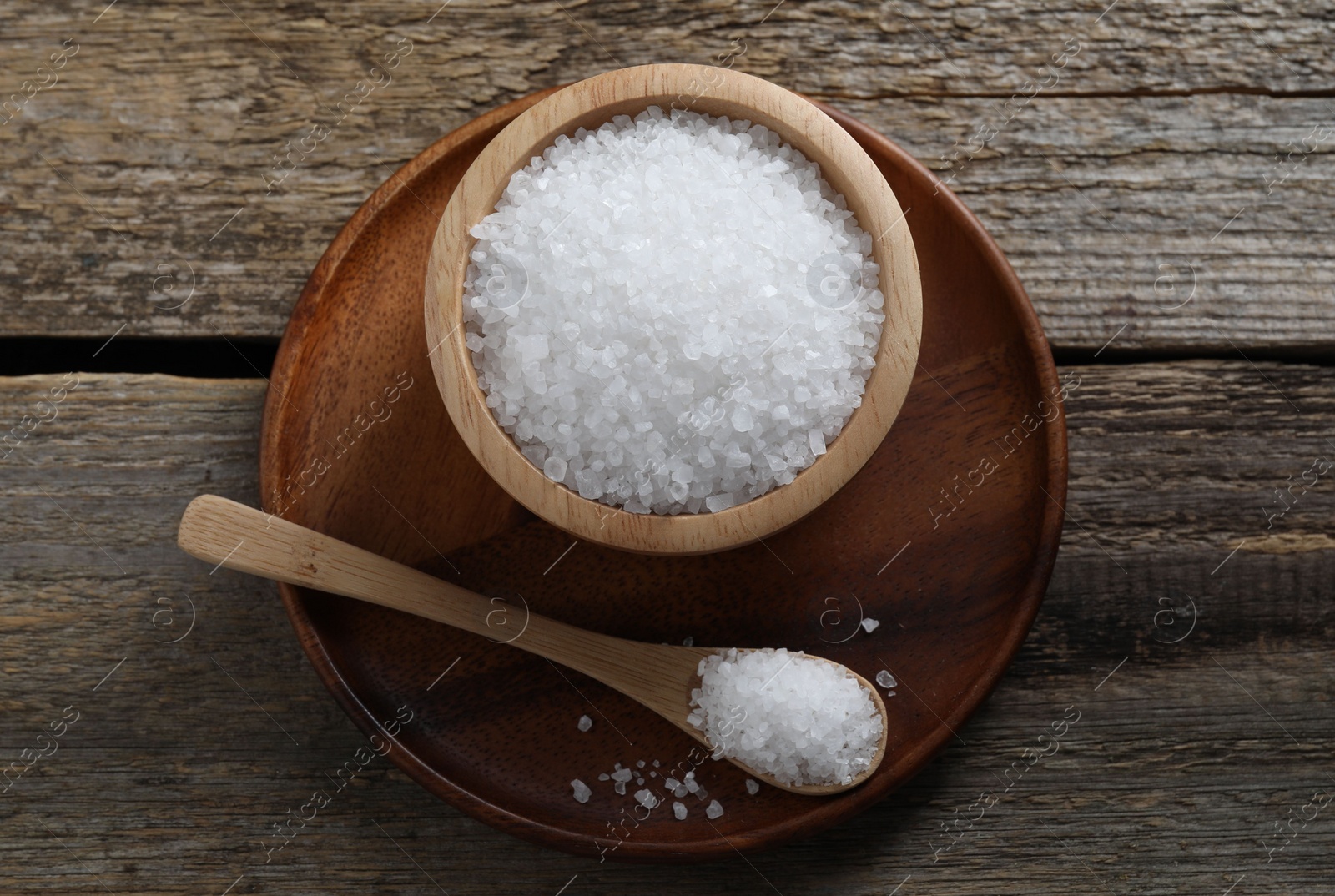 Photo of Organic salt in bowl and spoon on wooden table, top view