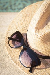 Photo of Stylish hat and sunglasses near outdoor swimming pool on sunny day, above view