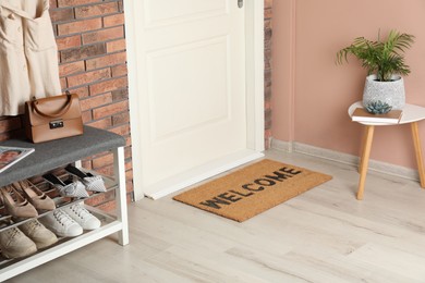 Photo of Doormat with word Welcome near shoe rack on white wooden floor in hall