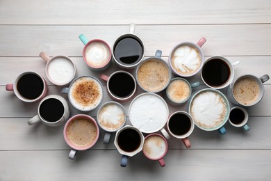 Many different cups with aromatic hot coffee on white wooden table, flat lay