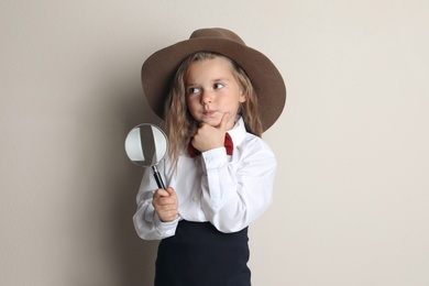 Cute little child in hat with magnifying glass playing detective on beige background