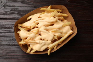 Photo of Tasty potato fries and cheese sauce in paper container on wooden table, top view