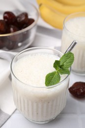 Glass of delicious date smoothie with mint on white table