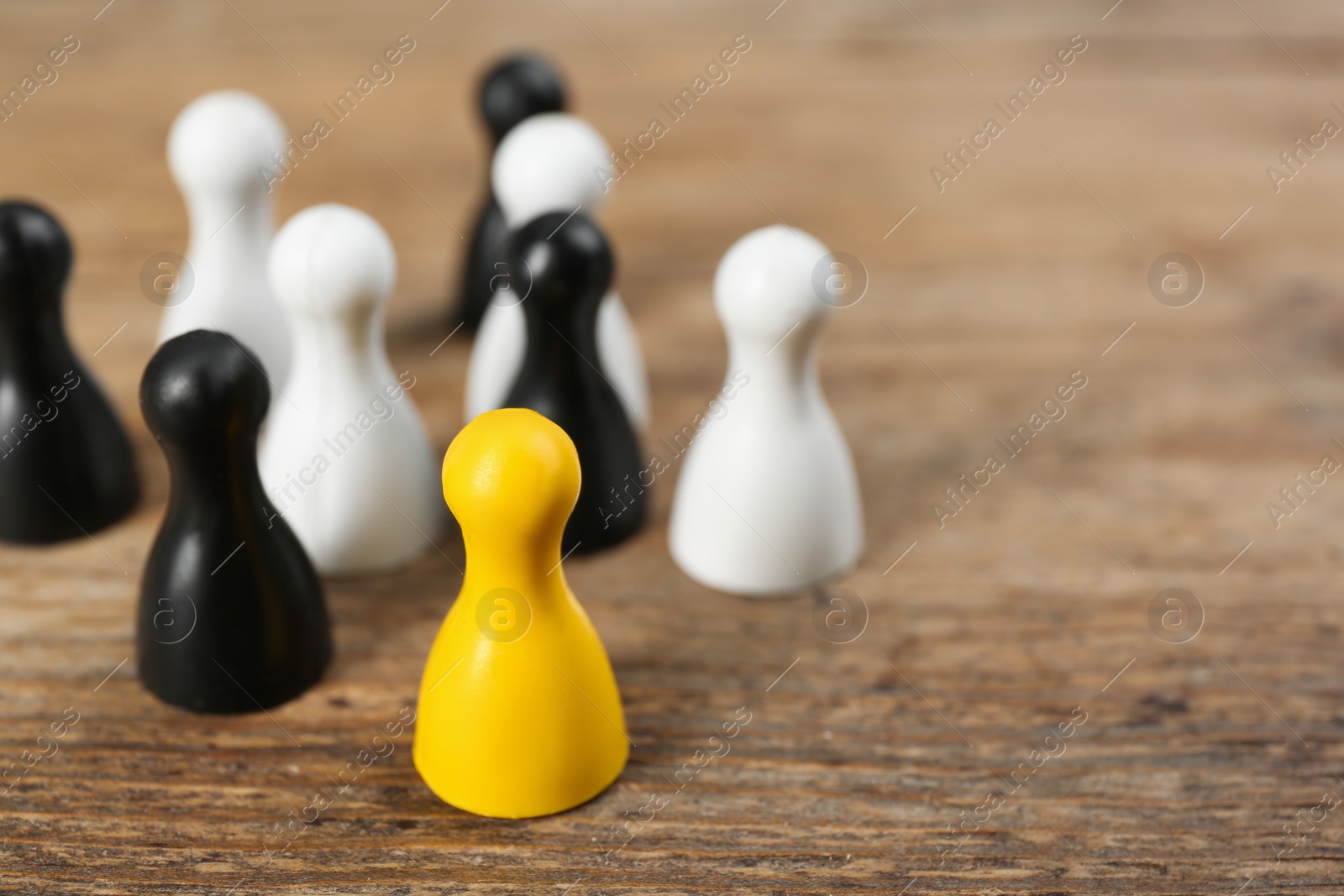 Photo of Yellow game piece among black and white ones on wooden background, closeup. Career promotion concept