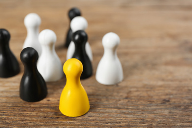 Yellow game piece among black and white ones on wooden background, closeup. Career promotion concept