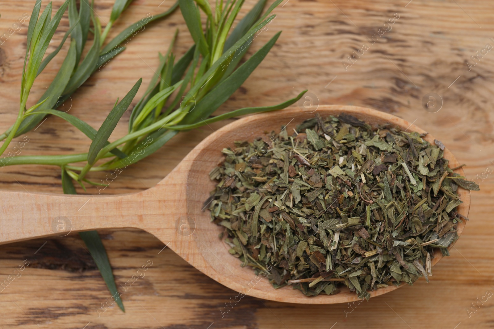 Photo of Spoon of dry tarragon and green leaves on wooden table, flat lay