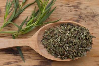 Spoon of dry tarragon and green leaves on wooden table, flat lay