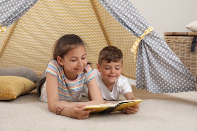 Photo of Cute little children reading book in toy wigwam at home