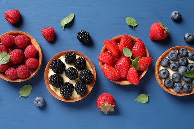 Photo of Tartlets with different fresh berries on blue wooden table, flat lay. Delicious dessert