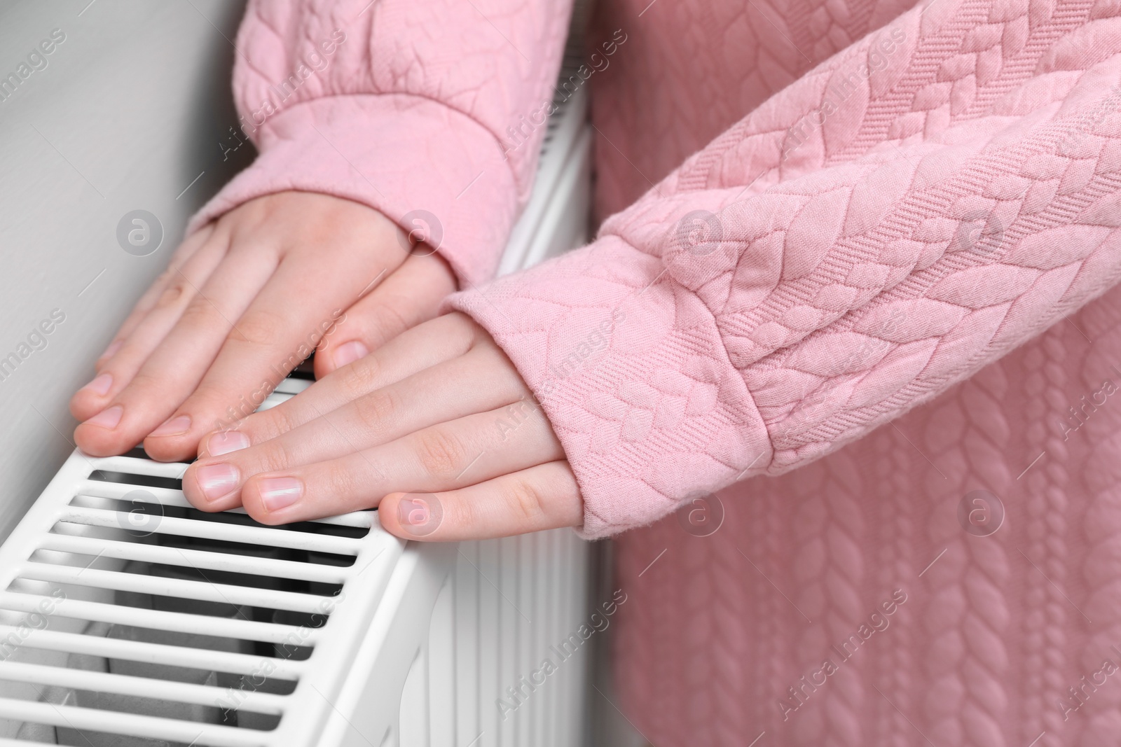 Photo of Girl warming hands on heating radiator indoors, closeup