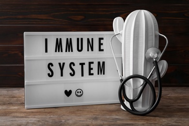 Photo of Lightbox with phrase Immune System, ceramic cactus and stethoscope on wooden table