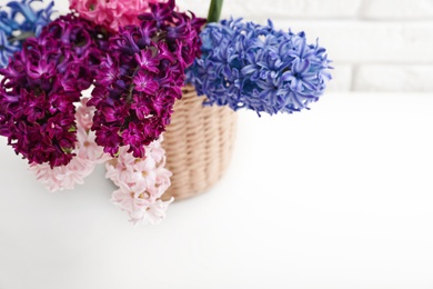 Photo of beautiful hyacinths in wicker pot on table, space for text. Spring flowers