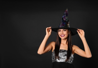 Photo of Beautiful woman wearing witch costume for Halloween party on black background, space for text