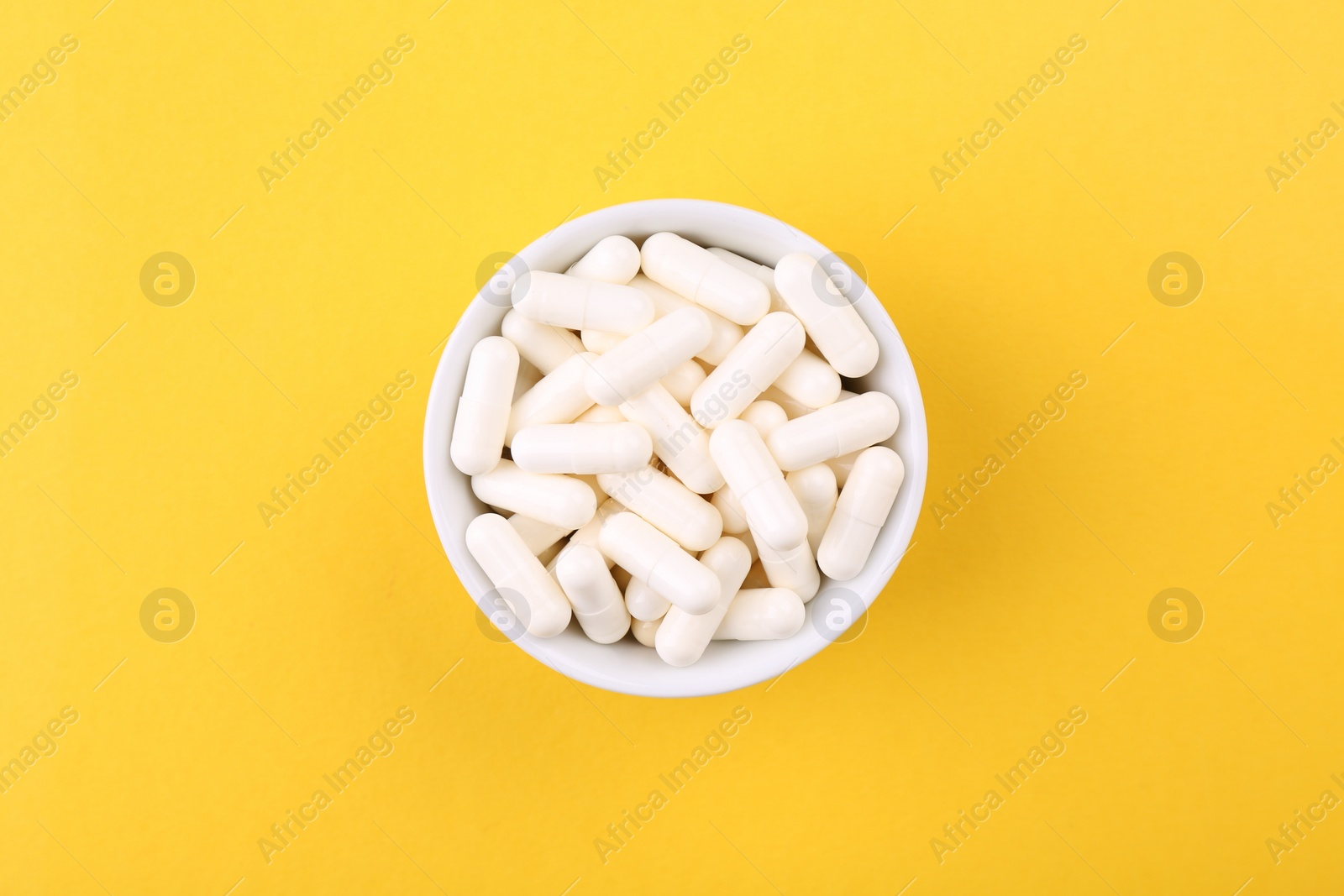 Photo of Vitamin capsules in bowl on orange background, top view