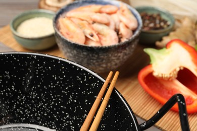 Black wok, chopsticks and bamboo mat with products on table, closeup