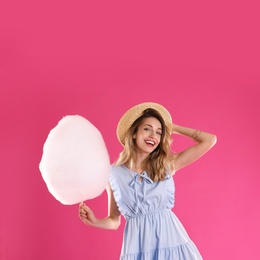 Happy young woman with cotton candy on pink background